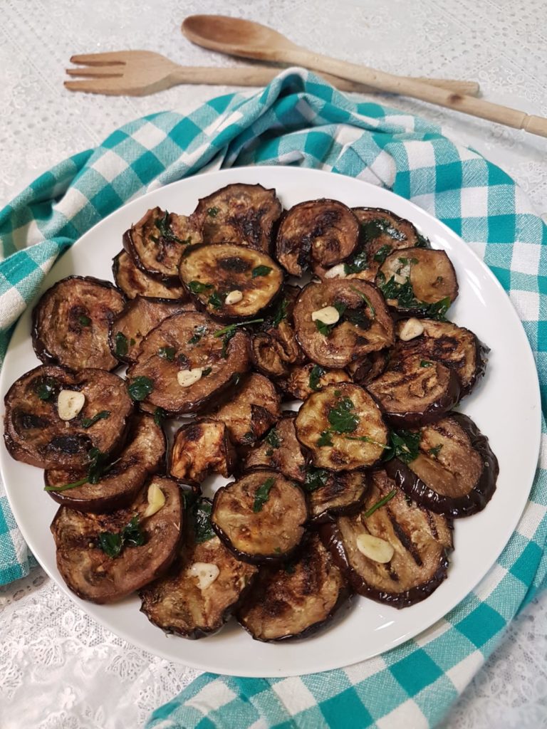 prato branco com fatias de berinjelas grelhadas sobre mesa com toalha xadrez....